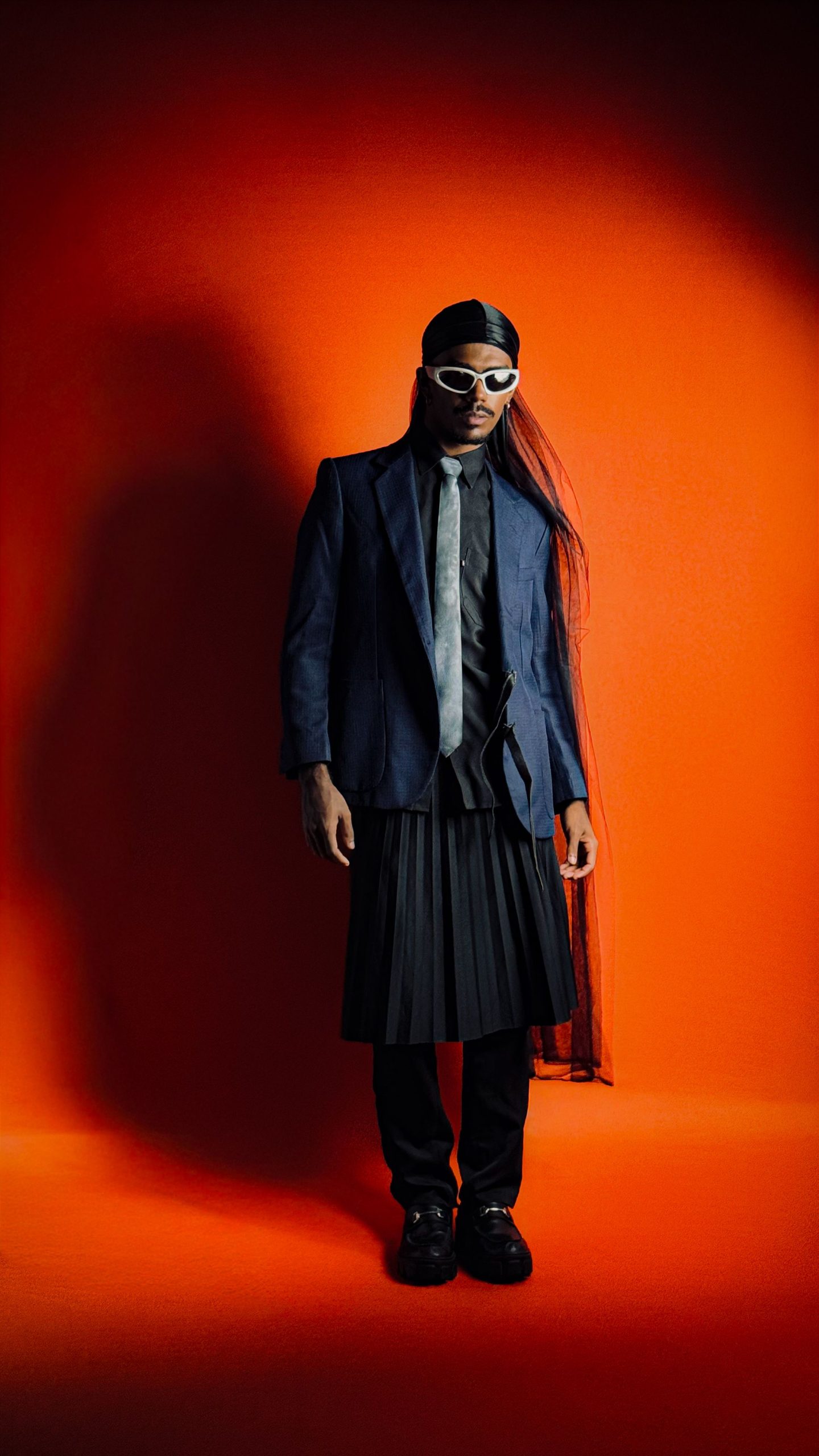 Model in dark avant-garde tailoring against a saturated orange backdrop