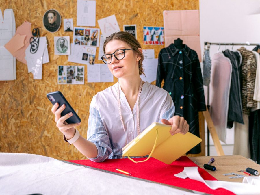 Fashion designer using a smartphone and notebook in a studio