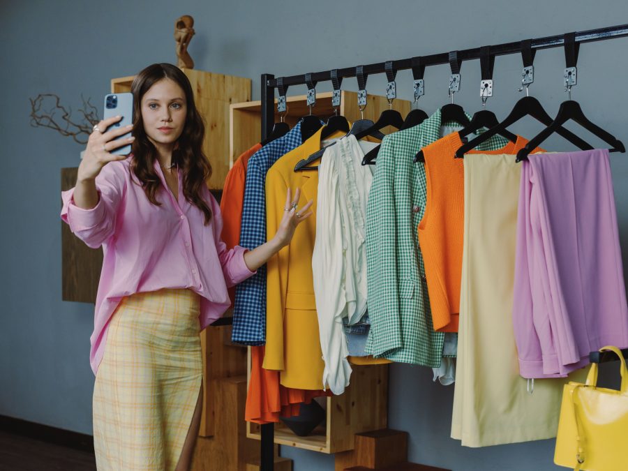 Shopper using a smartphone beside colorful clothes, illustrating virtual try on technology